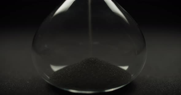 Black sand pouring inside hour glass