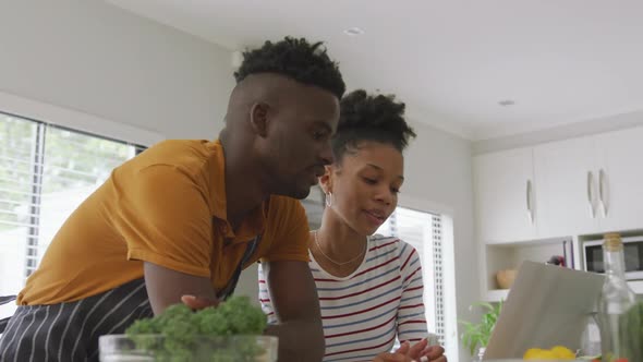 Video of happy african american couple cooking together in kitchen with tablet
