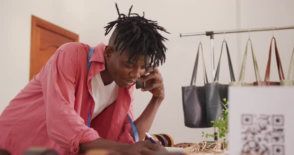 Happy african american craftsman with dreadlocks on phone call, taking an order at leather workshop