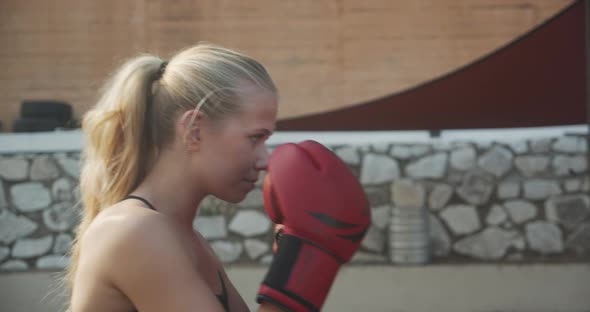 Woman Punching Bag In Boxing Gloves In Outdoor Gym