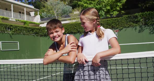 Portrait of caucasian brother and sister smiling together while standing at at tennis court on