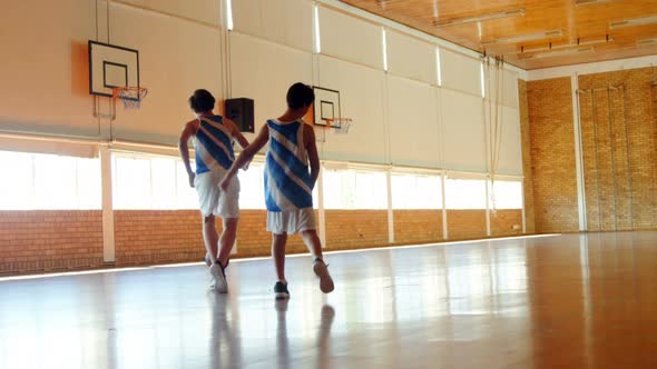 Two schoolboys playing basketball in basketball court