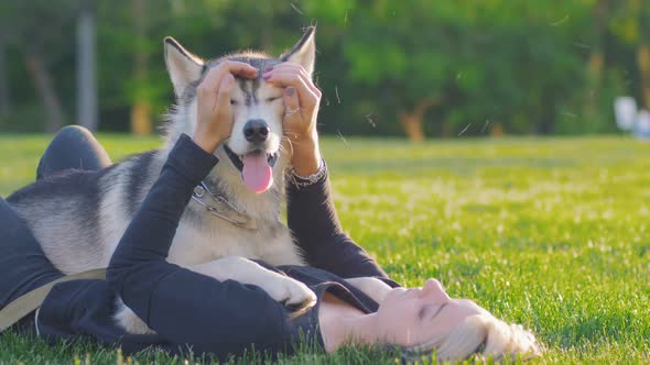 Beautiful Young Woman Playing with Funny Husky Dog Outdoors in Park