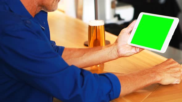 Mature man using digital tablet while having beer