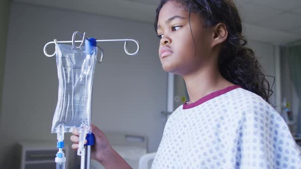 Mixed race girl standing with drip bag in hospital room