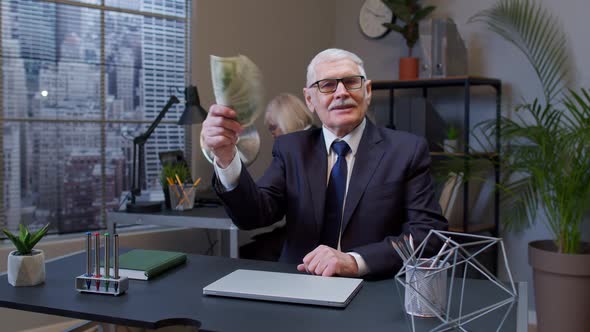 Smiling Senior Business Man Waving with Stack of Money at Office Workplace After Success Online Work