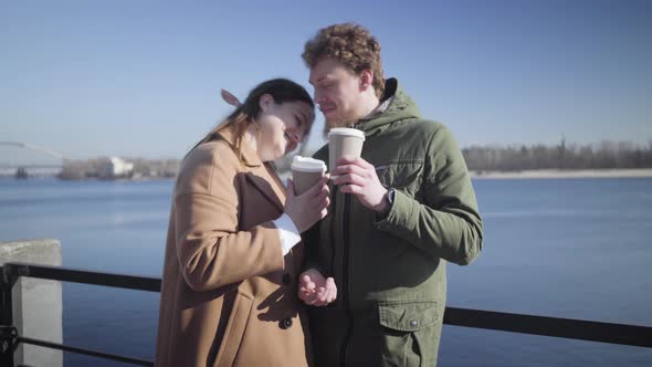 Portrait of Young Couple in Love Drinking Coffee on River Bank. Happy Caucasian Man and Woman Dating