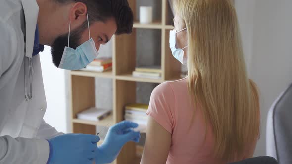 Male Doctor in Face Mask Making Coronavirus Vaccine Injection to Woman Patient