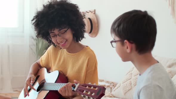 Afro American Woman Teaching Schoolchild to Play Guitar While Sitting on Bed at Home