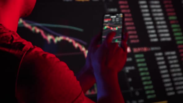 Trader Analyzes Cryptocurrency Charts on a Smartphone Screen in the Dark