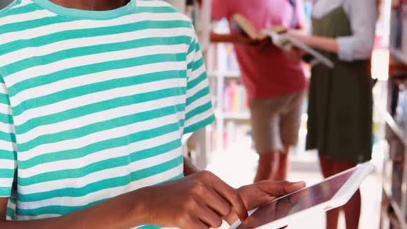 Smiling schoolboy using digital tablet in library