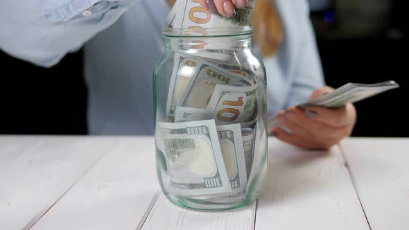 Closeup of Woman Hands Putting Dollar Money Into Glass Jar