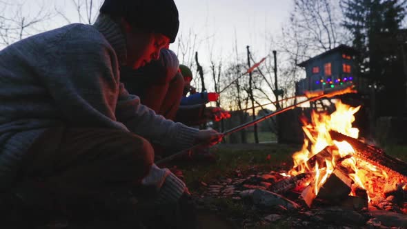 Two boys and their mother sitting around a bonfire with stick bread