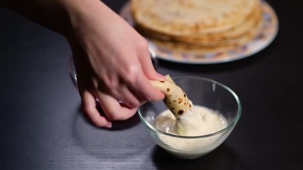 the girl s hand takes a twisted pancake and carefully dips it in sour cream