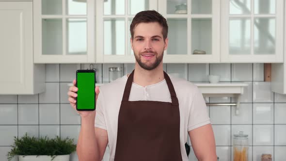 A Man in an Apron Holds a Smartphone with a Green Screen in His Hand