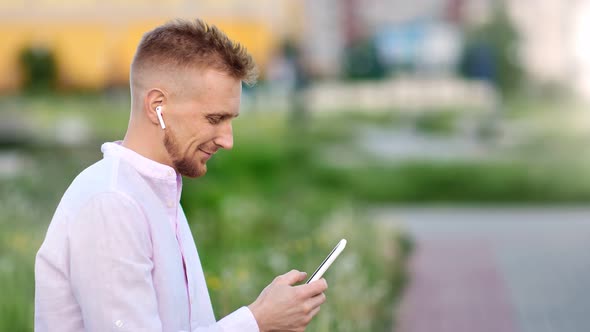 Happy Young Handsome Man Listening Music Wearing Wireless Earphones Using Smartphone