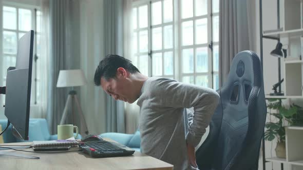 Asian Man Having Backache While Using Desktop Computer For Working At Home