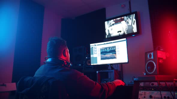 A Man Sound Engineer in Headphones Editing the Recorded Track of a Man Rapper