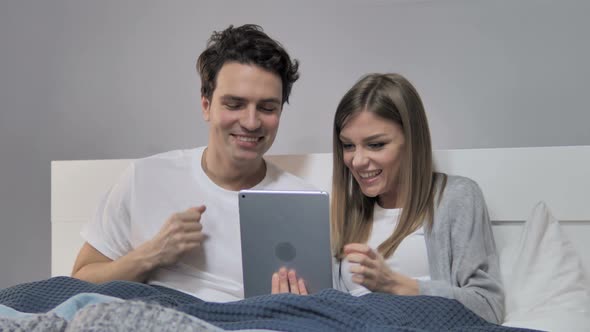 Young Couple Cheering for Win while Using Tablet in Bed