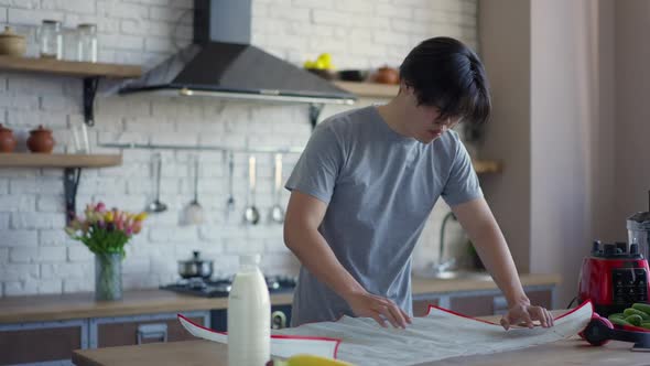 Professional Asian Male Landscaper Analyzing Blueprint Project Standing at Kitchen Table in Home