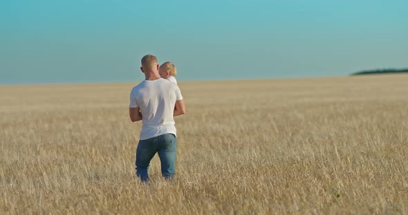 Young Man Carries a Baby Daughter in His Arms and Plucks Ears of Wheat