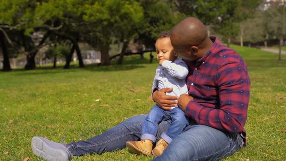 Father Raising Up Boy From Grass, Making Him Seated on Knees 