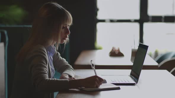 Asian Woman Working on Her Laptop and Writing in His Notebook Sitting at a Table