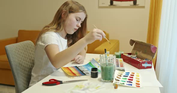 Girl Thoughtfully Draws a Picture with Colored Paints at Home.