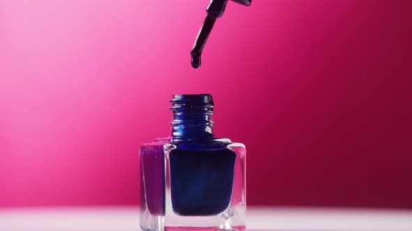 Blue Nail Polish Dripping Into Bottle on Pink Background