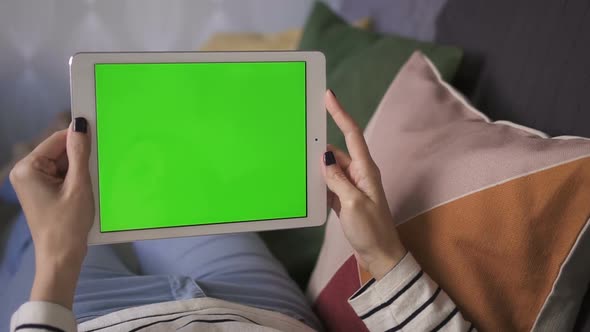 Business Digital Asian Woman Holding a Mockup Green Screen Tablet, on Couch at Home