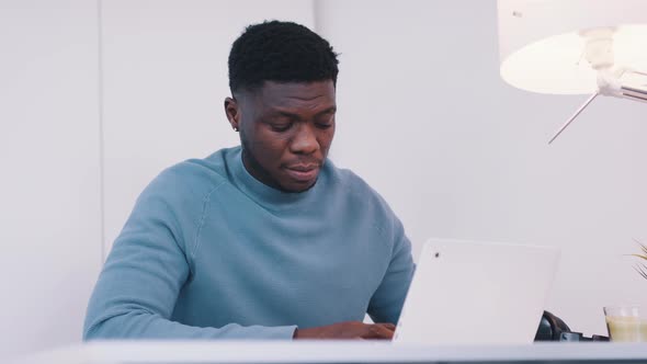 African American Black Man Sitting at the Table in Front of a Laptop  Stressed Out Using Smartphone