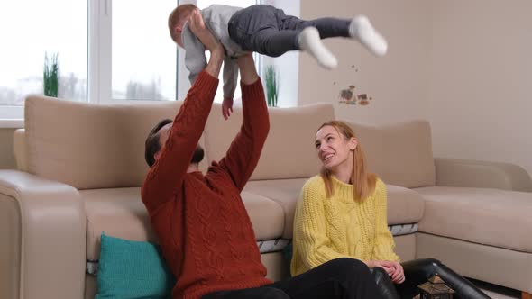 Happy Young Parents are Smiling Hugging and Playing with Their Little Son