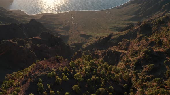 Aerial dolly tilt down over sunlit caldera Las Playas of ocean coast