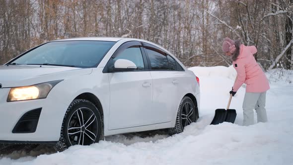 Female Digging Snow with Shovel Near Stuck Car