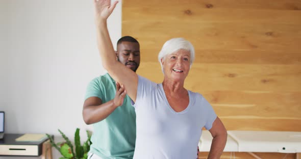 Video of happy african american male physiotherapist examining caucasian senior woman