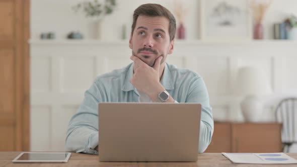 Young Man Thinking While Working on Laptop in Office