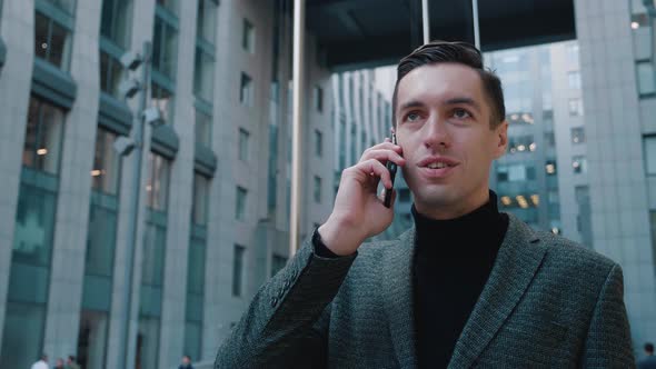 Successful Smiling Businessman Is Talking on Smartphone Outdoors Near Modern Building. Young Man Is