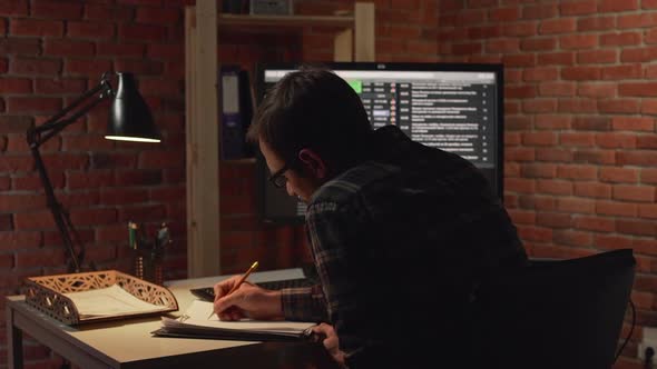 Back View of Caucasian Male Looking at Monitor with Spreadsheets Than Making Notes and Wearily