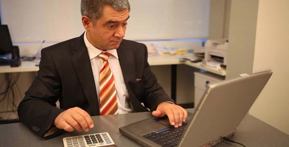 Businessman Using Laptop In Office, Calculating