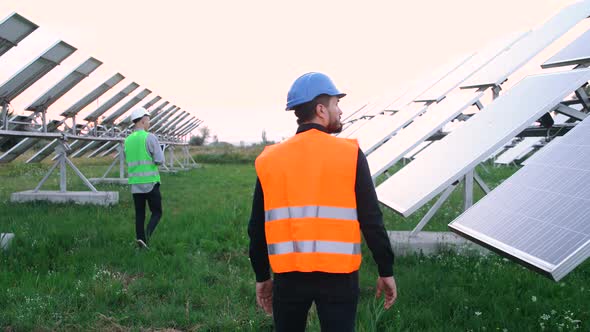 Two Old Construction Engineers Walk Between the Solar Panels on the Ecological Station.