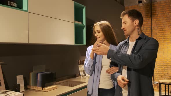 Couple Browsing Samples of Furniture in Modern Kitchen Showroom, They Discuss the Material