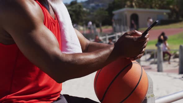 Senior african american man with basketball using smartphone near the beach
