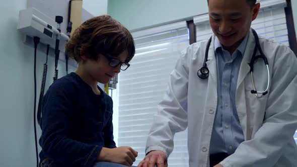 Front view of young asian male doctor examining caucasian boy patient knee in a clinic 4k