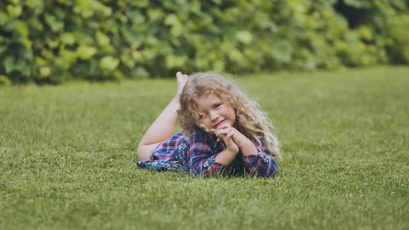 A Little Curlyhaired Girl Lies on the Grass in the Garden