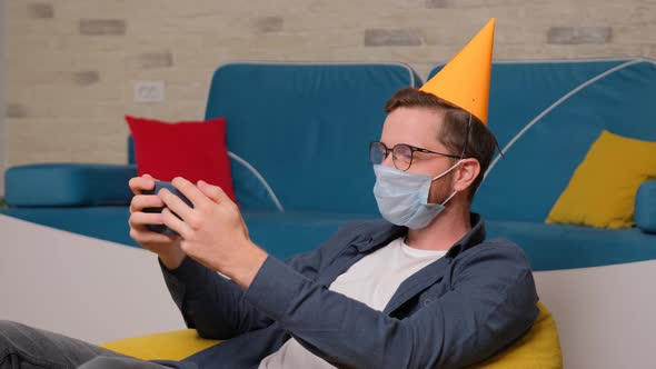 A Young Man with a Birthday Hat and a Medical Mask on His Face Talks Online with His Friends.