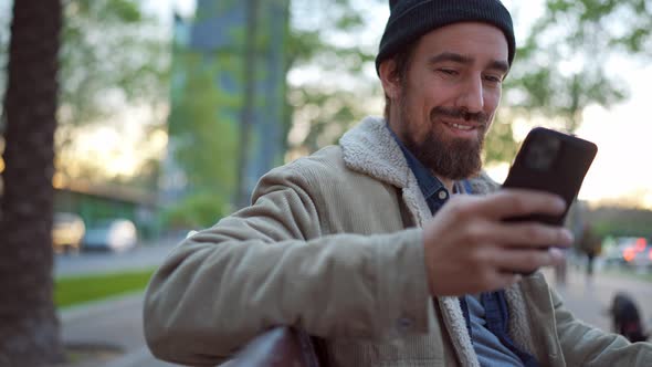 Positive man wearing hat texting on phone