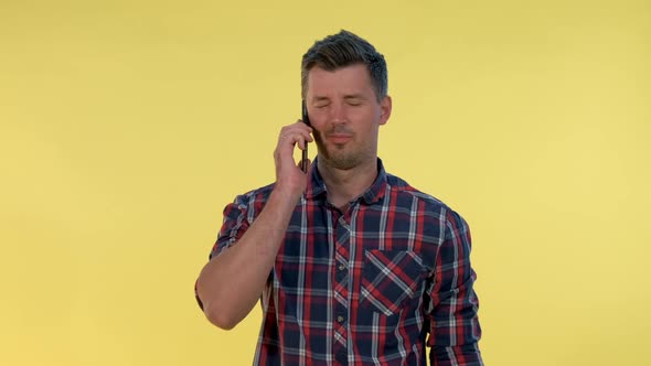 Pleasant-looking Young Man Speaking with Somebody By Smartphone on Yellow Background.
