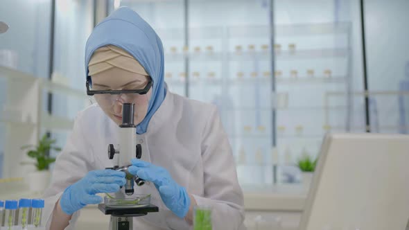 Muslim Scientist in a Modern Laboratory Works on a Laptop and a Microscope alt