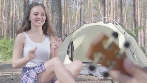 Unrecognized Man Playing Ukulele at the Tent While Pretty Young Happy Woman Sitting in Front of Him