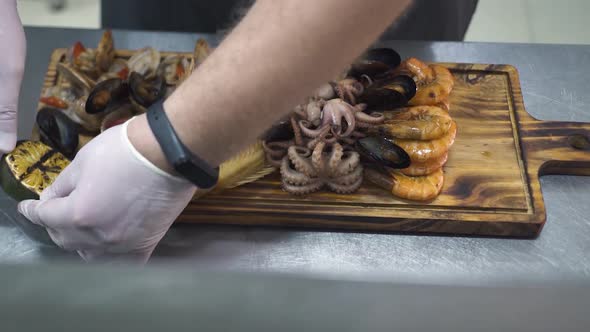 Man Puts Grilled Orange on Board with Sea Delicacies Closeup